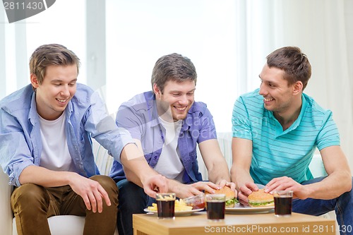 Image of smiling friends with soda and hamburgers at home