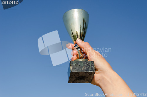 Image of female hand hold award cup on blue sky background 