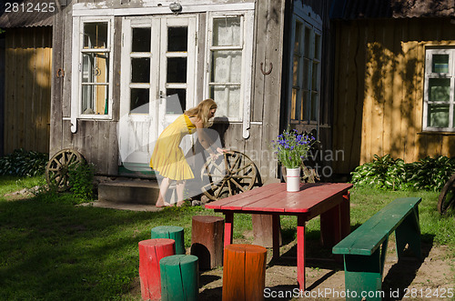 Image of Rural house yard and girl roll old carriage wheel 