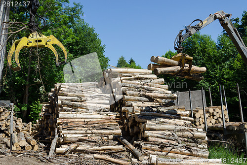 Image of Crane claw and stack of logs near truck trailer 