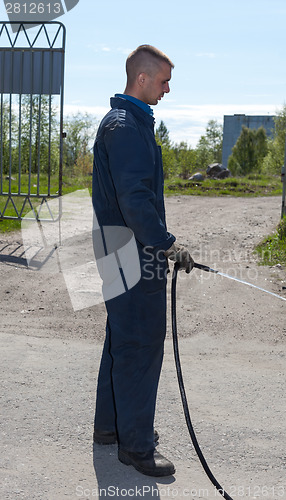 Image of Worker in overalls watering area with water from a hose 