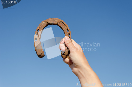 Image of hand hold vintage horseshoe on blue sky background 