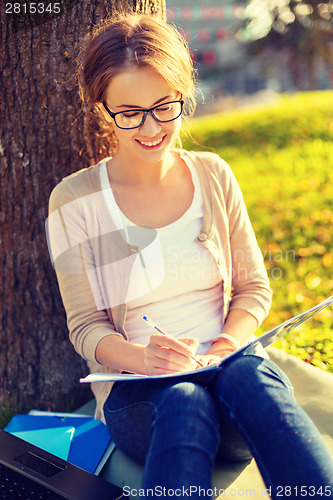Image of smiling teenager in eyeglasses writing in notebook