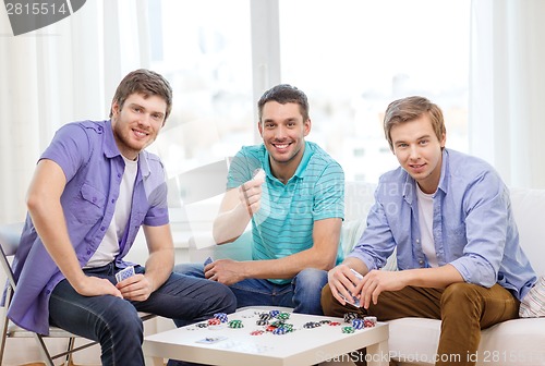 Image of happy three male friends playing poker at home