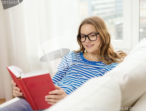 Image of smiling teenage girl reading book on couch