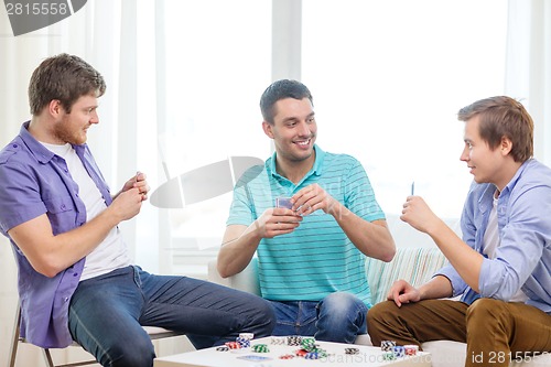 Image of happy three male friends playing poker at home