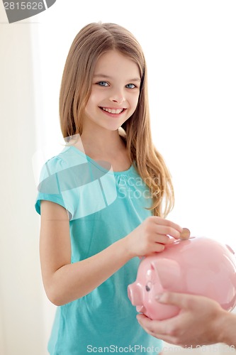 Image of smiling little girl putting coin into piggy bank