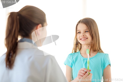 Image of female doctor giving toothbrush to smiling girl