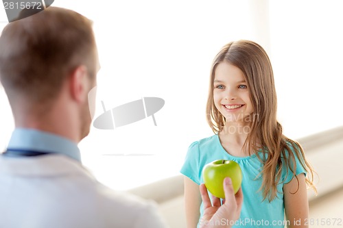 Image of male doctor giving an apple to smiling little girl