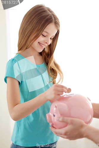 Image of smiling little girl putting coin into piggy bank