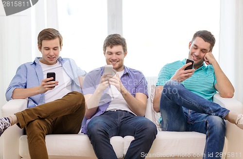 Image of smiling friends with smartphones at home