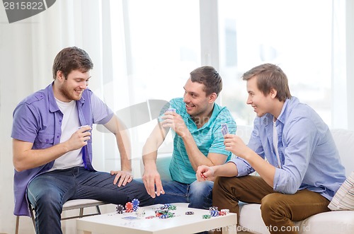 Image of happy three male friends playing poker at home