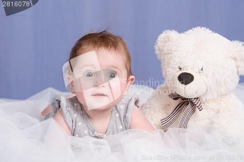 Image of Six-month baby girl with teddy bear lying on couch