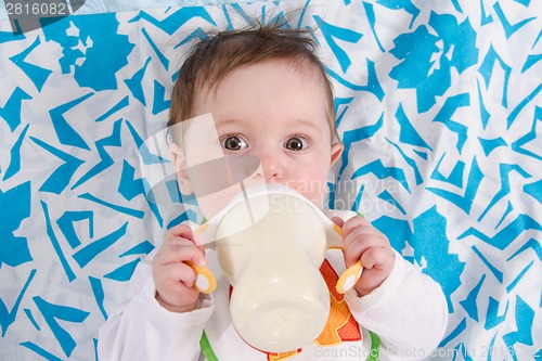 Image of Baby lying in crib and drinking milk from a bottle