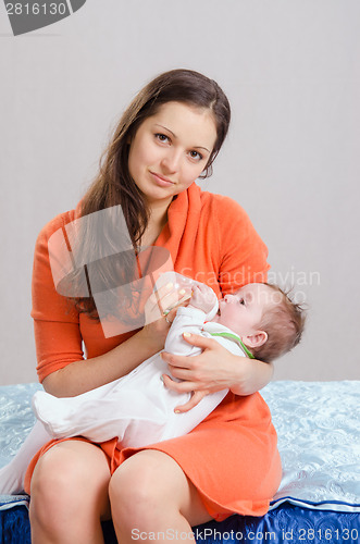 Image of Mum feeds from a bottle six-month daughter sitting on bed