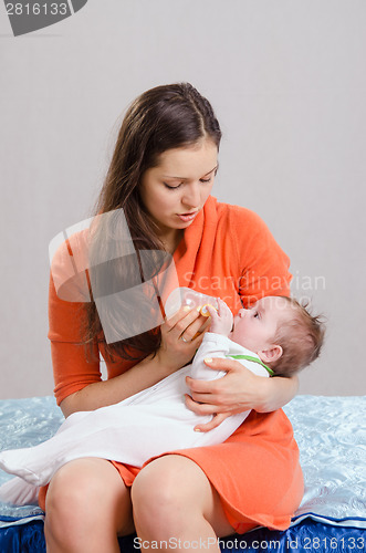 Image of Mum feeds from bottle daughter sitting on a bed