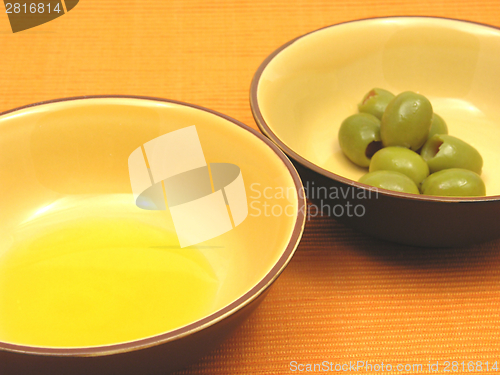 Image of Two bowls of ceramic with olive oil and olives on orange background