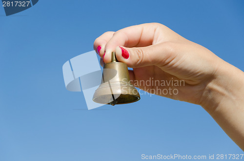Image of Woman hand red nails hold iron bell on blue sky 