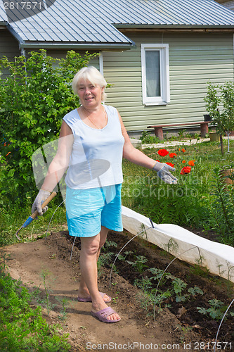 Image of Elderly woman stands in the midst of the garden