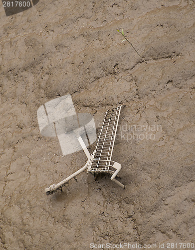 Image of shopping cart dumped in mud at side of river