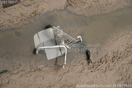 Image of shopping cart dumped in mud at side of river