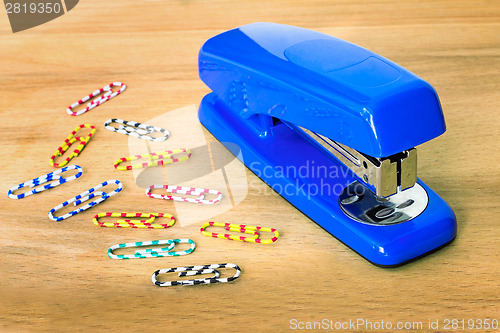 Image of Stapler of bright blue color and paper clip against a table.