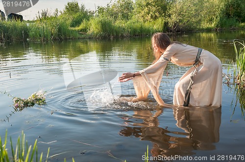 Image of Attractive girl lowers wreath in water