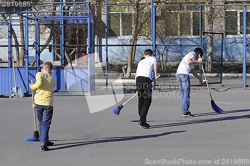 Image of Teenagers sweep the yard with sweepers during a community work d
