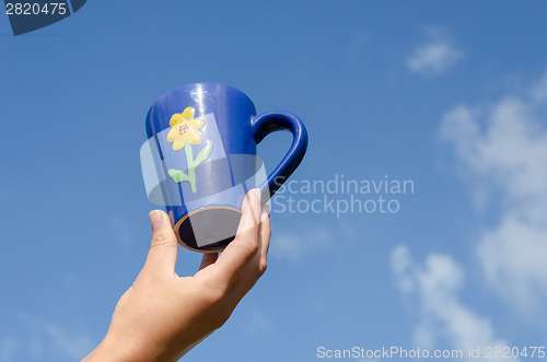 Image of blue clay cup flower in hand blue sky background 