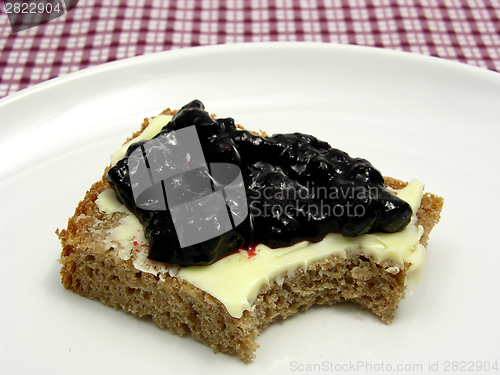 Image of Bitten into a wholemeal butterbread  with bilberry jam placed on a round plate arranged on a placemat