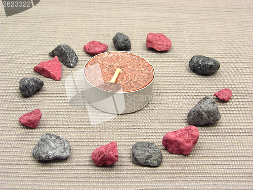 Image of Tea candle surrounded by decoration stones on a brown background
