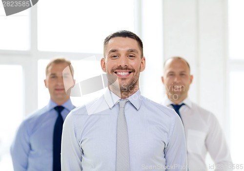 Image of smiling businessman in office with team on back