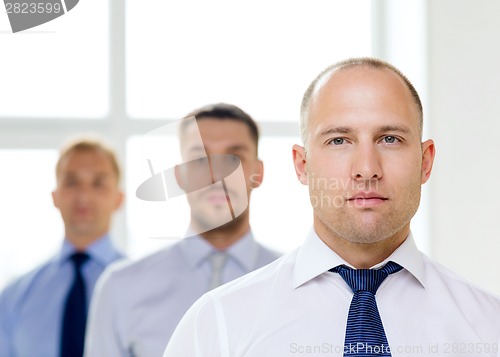 Image of serious businessman in office with team on back