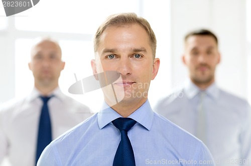 Image of serious businessman in office with team on back