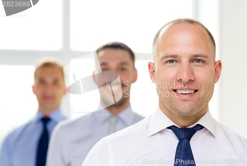 Image of smiling businessman in office with team on back