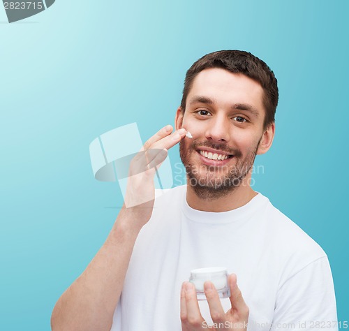 Image of beautiful smiling man applyin cream