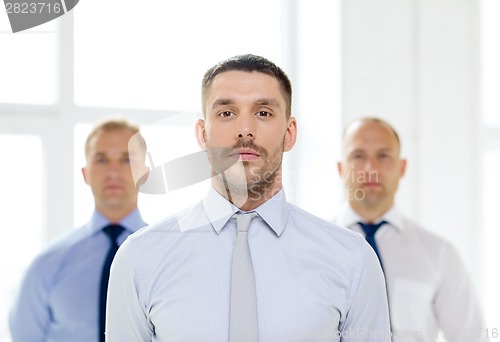 Image of serious businessman in office with team on back