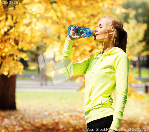 Image of woman drinking water after doing sports outdoors