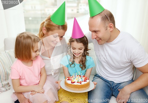 Image of smiling family with two kids in hats with cake