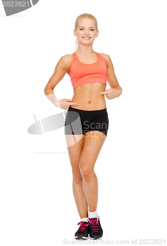 Image of smiling sporty woman pointing at her six pack