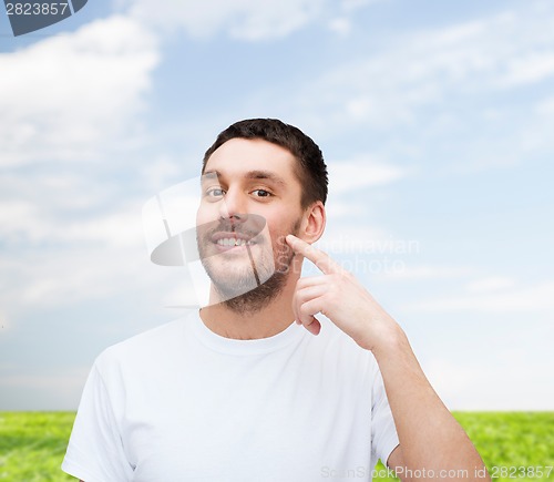 Image of smiling young handsome man pointing to cheek