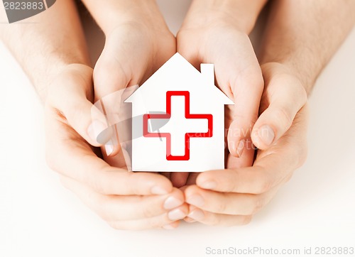 Image of hands holding paper house with red cross