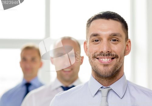 Image of smiling businessman in office with team on back