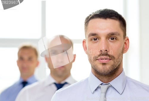 Image of serious businessman in office with team on back