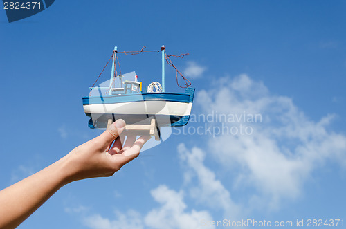 Image of female hand hold wooden ship toy on sky background 