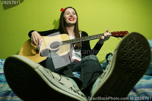 Image of Young brunette playing guitar on bed