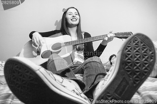 Image of Young brunette playing guitar on bed black and white