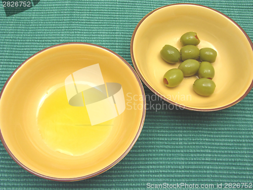 Image of Two bowls of ceramic with olive oil and olives on green background