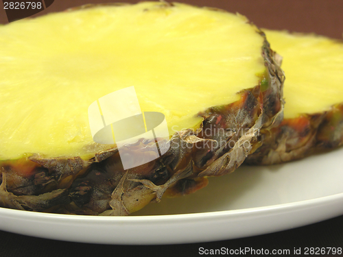 Image of Two slices of pineapple on a white plate and brown placemat