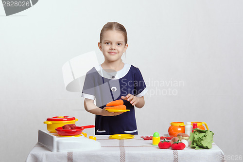 Image of Girl with a plate of carrots on toy kitchen
